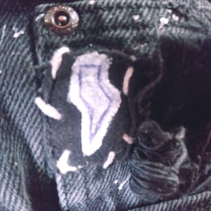 Peut inclure: Gros plan sur une poche en jean noir avec un patch en forme d'&eacute;clair blanc et bleu. La poche a un bouton en m&eacute;tal et est partiellement d&eacute;chir&eacute;e.