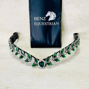 Puede incluir: Una cabezada ecuestre negra con un diseño decorativo de cristales verdes y transparentes. Los cristales están dispuestos en forma de hojas. Una bolsa negra con el texto "BENZ EQUESTRIAN" está en el fondo.