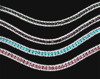 May include: Four curved rhinestone chains arranged in parallel rows. Each chain features a central row of coloured stones—dark green, deep purple, bright turquoise, and light pink—flanked by two outer rows of small, clear, sparkling rhinestones.
