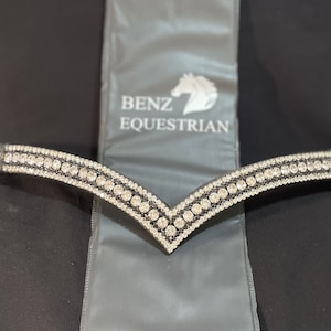 May include: A black leather horse browband with a V-shaped design featuring rows of clear rhinestones. The browband is labelled "Benz Equestrian".