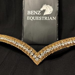 Puede incluir: Un frontal de caballo dorado y cristal transparente. El frontal tiene un diseño en V con dos filas de cristales.