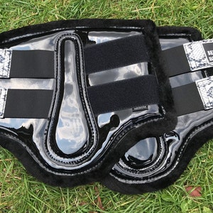 May include: Pair of black and white horse leg boots with a snake print design and the text "Benz Equestrian" on the straps.