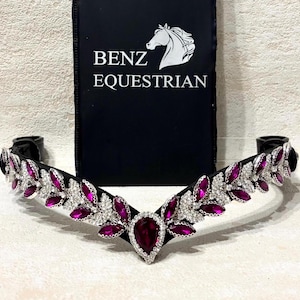 Puede incluir: Una cabezada ecuestre negra con un diseño decorativo. La cabezada presenta gemas de color magenta y cristales transparentes. El nombre de la marca "BENZ EQUESTRIAN" está impreso sobre un fondo negro.