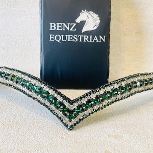 May include: A green and silver horse browband with crystal embellishments. The browband is shaped like a V and has a silver base. The browband is made by Benz Equestrian.