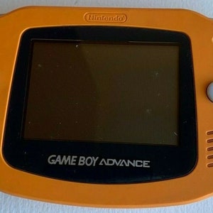 May include: An orange Game Boy Advance handheld video game console with a black screen and white buttons. The console has the text "GAME BOY ADVANCE" printed on the front.
