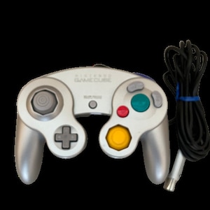 May include: A silver Nintendo GameCube controller with a black cord and a white plug. The controller has a yellow, red, and blue button.