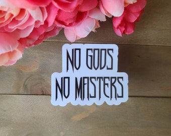 Puede incluir: Pegatina blanca con texto negro que dice "NO GODS NO MASTERS". La pegatina está sobre una superficie de madera.