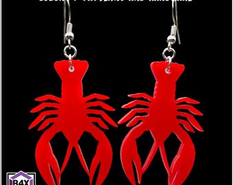 May include: A pair of bright red lobster-shaped earrings with silver-colored hooks. The earrings are cut from a solid material and feature the text "AVAILABLE IN MANY COLORS / PATTERNS AND HARDWARE". The earrings are displayed against a black background.