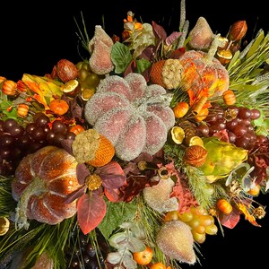 Puede incluir: Un arreglo oto&ntilde;al con calabazas, uvas y peras. La exhibici&oacute;n presenta calabazas naranjas y marrones, uvas moradas y verdes, y peras espolvoreadas con purpurina. El fondo es oscuro.