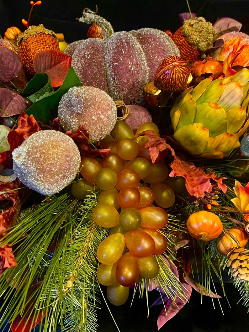 Puede incluir: Un arreglo con tem&aacute;tica oto&ntilde;al con una calabaza grande y escarchada, orbes azucarados y un racimo de uvas verdes y &aacute;mbar. El arreglo incluye agujas de pino, hojas de oto&ntilde;o y peque&ntilde;as calabazas en tonos naranja, rojo y verde.