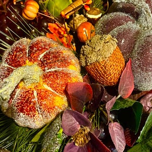 Puede incluir: Primer plano de un arreglo oto&ntilde;al con una calabaza grande y naranja con purpurina, una bellota y varias hojas. El arreglo incluye peque&ntilde;as calabazas, bayas y vegetaci&oacute;n, creando una exhibici&oacute;n festiva.