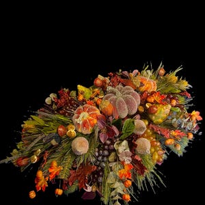 Puede incluir: Un vibrante arreglo oto&ntilde;al con calabazas, uvas y follaje de oto&ntilde;o. La exhibici&oacute;n incluye elementos naranjas, morados y verdes, creando una composici&oacute;n festiva y colorida sobre un fondo negro.