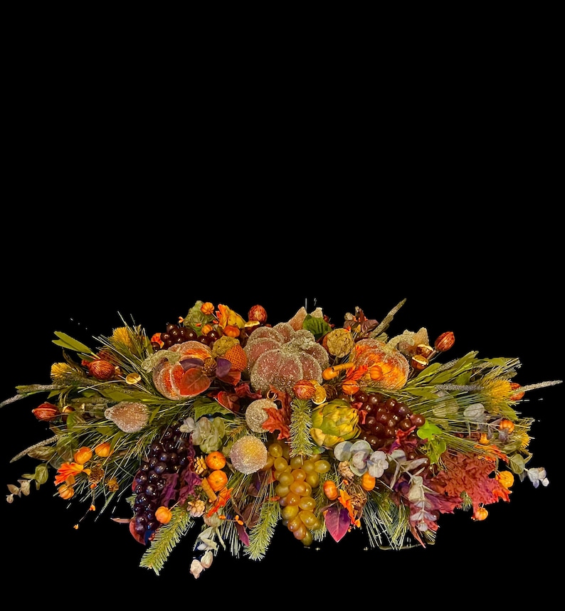 Puede incluir: Un centro de mesa con tem&aacute;tica oto&ntilde;al con calabazas, uvas y varios follajes. El arreglo presenta elementos naranjas, marrones y verdes, creando una exhibici&oacute;n festiva y decorativa. El centro de mesa est&aacute; sobre un fondo negro.
