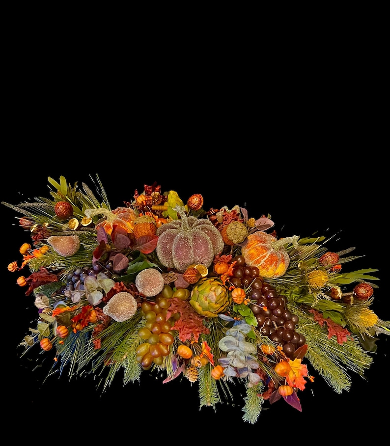 Puede incluir: Un centro de mesa con tem&aacute;tica oto&ntilde;al con calabazas, uvas y follaje variado. El arreglo presenta elementos naranjas, marrones y verdes, incluyendo agujas de pino, bayas y calabazas decorativas. El centro de mesa est&aacute; sobre un fondo negro.