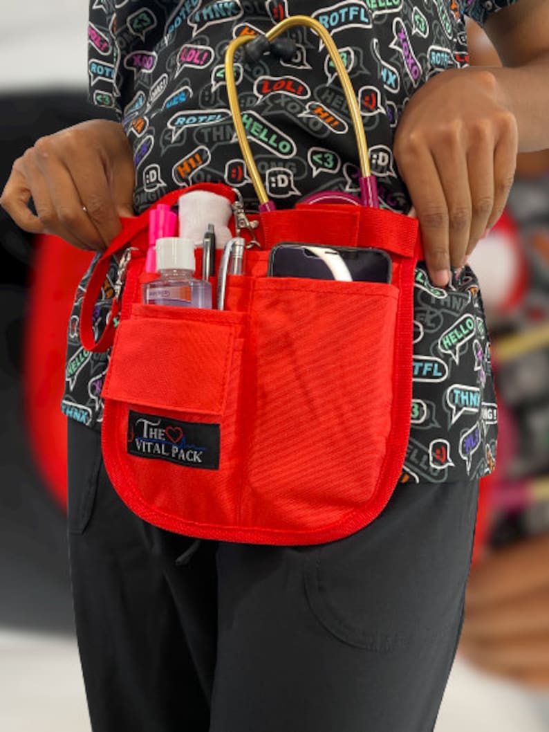 May include: Red medical utility belt with multiple pockets and a phone holder. The belt has a black patch with the text "The Vital Pack" and a heart symbol.