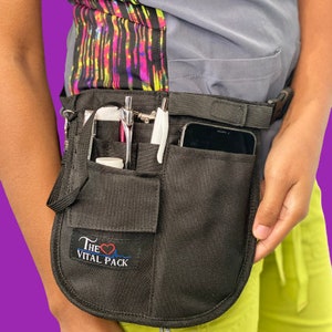 May include: Black medical utility belt with multiple pockets and a phone holder. The belt has a logo that says "The Vital Pack" with a heart and EKG line.