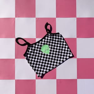 May include: Black and white checkered crop top with a green heart graphic. The top has thin black straps.
