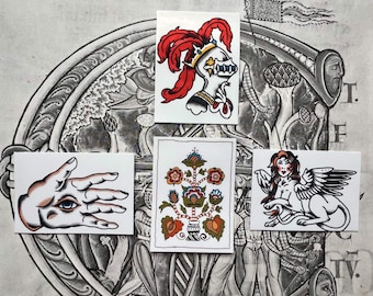 May include: Four rectangular stickers featuring traditional tattoo-style illustrations: a knight in a helmet with red plumes, a hand with an eye in the palm, a symmetrical floral tree design, and a winged sphinx with long hair and dark wings.
