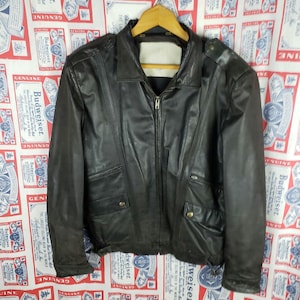 May include: A black leather jacket with a zip-up front, a collar, and multiple pockets. The jacket is hanging on a wooden hanger. The background features a patterned fabric with the Budweiser logo.