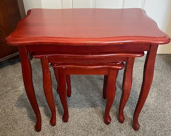 May include: A set of three nesting tables made of dark wood with a smooth, glossy finish. The tables have a curved top edge and are supported by four legs each.