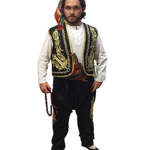 Puede incluir: Un hombre vistiendo un chaleco tradicional negro con bordados dorados, pantalones negros y un pañuelo de cabeza colorido. Está sosteniendo un rosario.