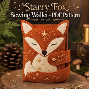 May include: A felt sewing wallet shaped like a fox with rust-orange and cream-colored fabric. The fox face features closed eyes and a black nose. Gold embroidered stars and swirling lines decorate the exterior. Text reads Starry Fox Sewing Wallet - PDF Pattern.