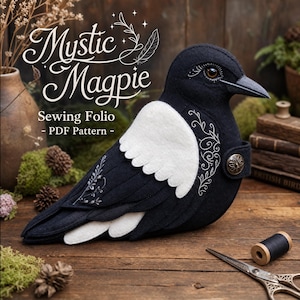 May include: A black and white felt magpie bird sewing folio with embroidered floral details, a dark brown eye, and a metallic button closure. The text Mystic Magpie Sewing Folio - PDF Pattern is displayed in white script and serif font above the bird.