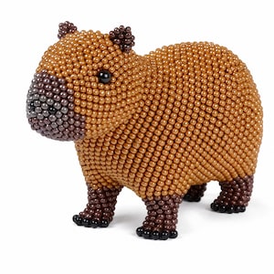 Puede incluir: Una pequeña figura de capibara hecha con numerosas cuentas diminutas y redondas con acabado metálico. El cuerpo es principalmente de color marrón claro, con el hocico, las orejas y las patas de color marrón oscuro. Tiene dos cuentas negras brillantes como ojos.