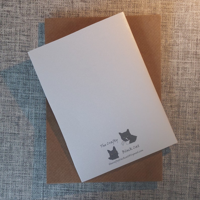 May include: A white rectangular greeting card resting on a brown envelope. The bottom right corner of the card features a black graphic of two cats and the text The Crafty Black Cat along with the email address thecraftyblackcat15@gmail.com.