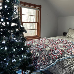 K&ouml;nnte beinhalten: Ein Schlafzimmer mit einem Weihnachtsbaum, der mit wei&szlig;en Lichtern geschm&uuml;ckt ist, und einem Bett mit einer bunten H&auml;keldecke.