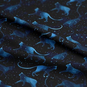Op de afbeelding: Een stof met een herhalend patroon van blauwe kattenconstellaties op een zwarte achtergrond. De katten worden in verschillende poses afgebeeld, met lijnen die constellaties verbinden. Witte stippen simuleren sterren, waardoor een hemels thema ontstaat.