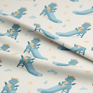 May include: A light-colored fabric featuring a repeating pattern of cartoon dragons on slides. The dragons are blue with orange accents, and the slides are a matching blue. Small clouds and trees are scattered throughout the design.