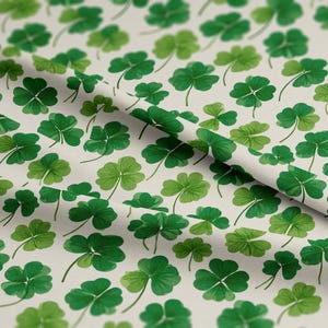 May include: A fabric featuring a repeating pattern of green shamrocks on a cream backdrop. The shamrocks vary in size and shade, creating a textured effect. Ideal for St. Patrick's Day or Irish-themed crafts and projects.