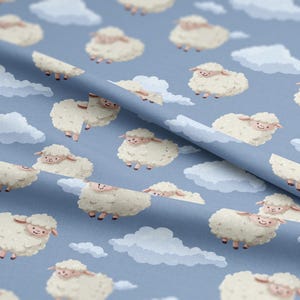 Op de afbeelding: Een lichtblauwe stof met een herhaald patroon van cartoon schapen en pluizige witte wolken. De schapen zijn wit met roze gezichten en poten. De wolken zijn in verschillende maten en vormen.