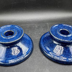 Pode incluir: Dois porta-velas de cerâmica azul com um esmalte salpicado. Cada porta-velas tem um anel central elevado para segurar uma vela.