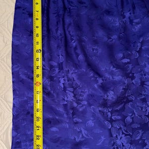 Peut inclure: Une jupe bleu vif avec un motif floral, mesurant environ 74 cm de long. Le tissu a un l&eacute;ger &eacute;clat, et la jupe est mesur&eacute;e avec un m&egrave;tre ruban jaune. Le motif floral se r&eacute;p&egrave;te sur toute la jupe.