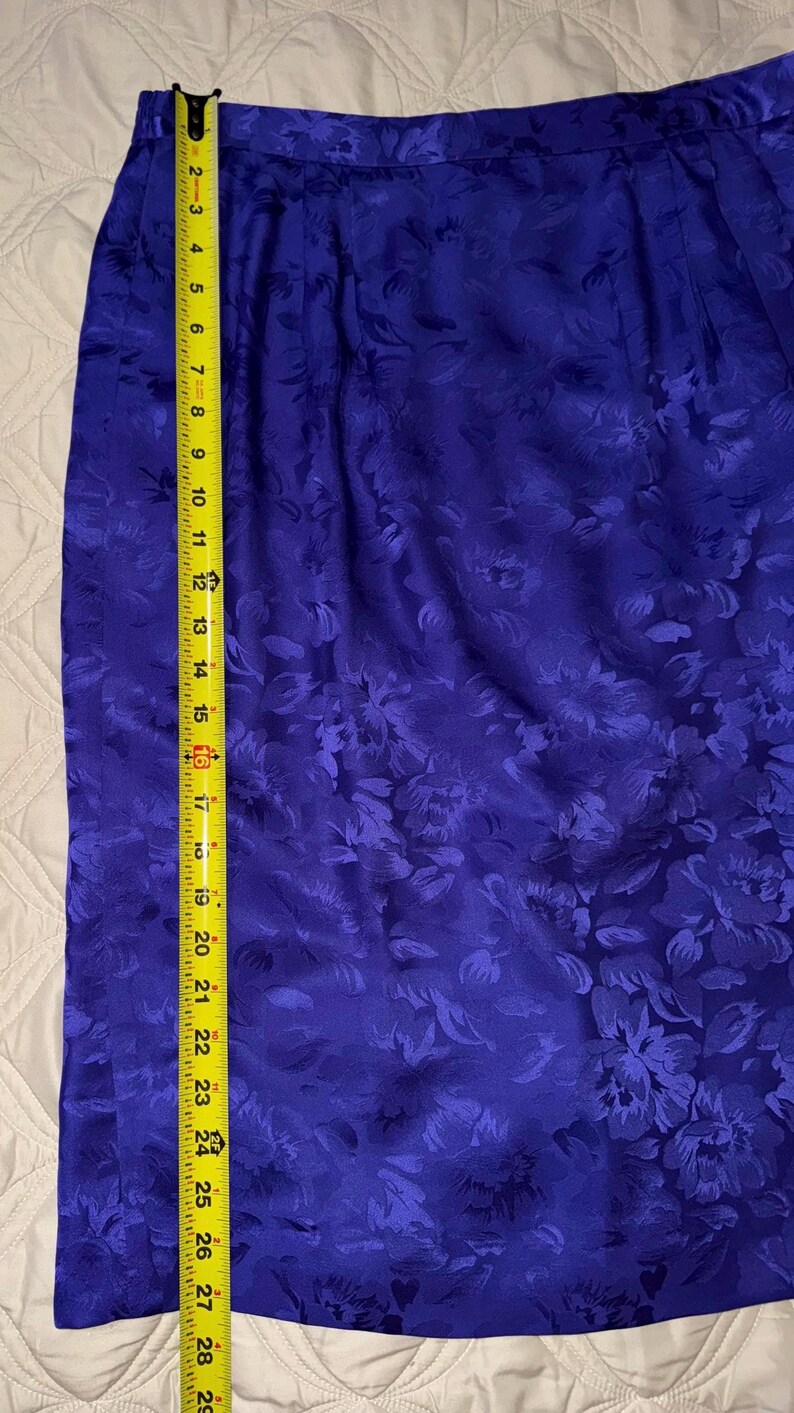 Peut inclure: Une jupe bleu vif avec un motif floral, mesurant environ 74 cm de long. Le tissu a un l&eacute;ger &eacute;clat, et la jupe est mesur&eacute;e avec un m&egrave;tre ruban jaune. Le motif floral se r&eacute;p&egrave;te sur toute la jupe.