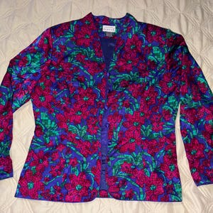 Peut inclure: Veste &agrave; manches longues &agrave; imprim&eacute; floral dans les tons de bleu, fuchsia et vert. La veste a un devant boutonn&eacute; et un col. Le motif floral est un motif r&eacute;p&eacute;titif de grandes fleurs et de feuilles. La veste est en mati&egrave;re soyeuse.