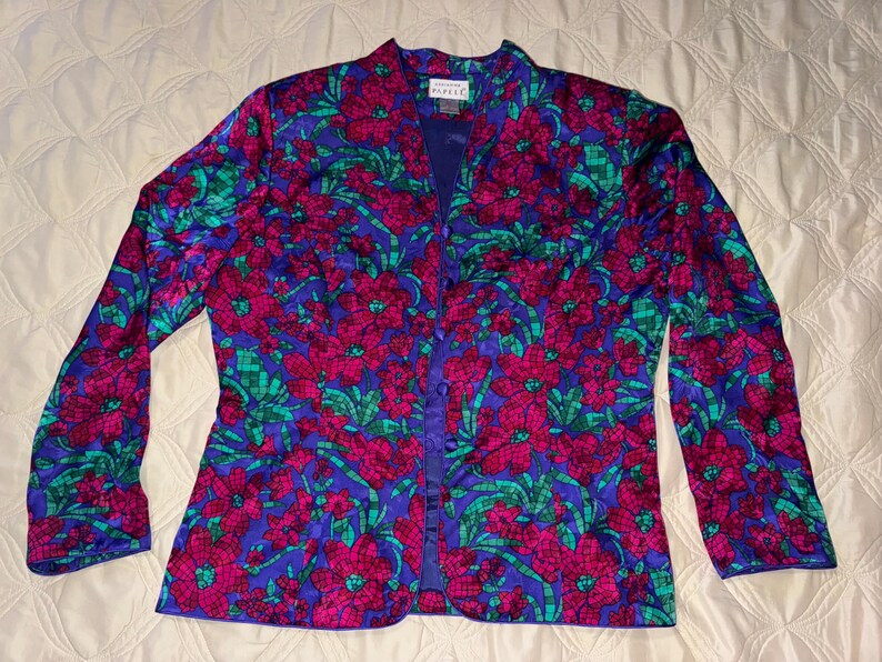 Peut inclure: Veste &agrave; manches longues &agrave; imprim&eacute; floral dans les tons de bleu, fuchsia et vert. La veste a un devant boutonn&eacute; et un col. Le motif floral est un motif r&eacute;p&eacute;titif de grandes fleurs et de feuilles. La veste est en mati&egrave;re soyeuse.