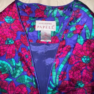 Peut inclure: Veste aux motifs floraux vibrants dans les tons de violet, fuchsia et sarcelle. La veste pr&eacute;sente une encolure en V et un imprim&eacute; floral audacieux. L'&eacute;tiquette indique "Adrianna Papell".