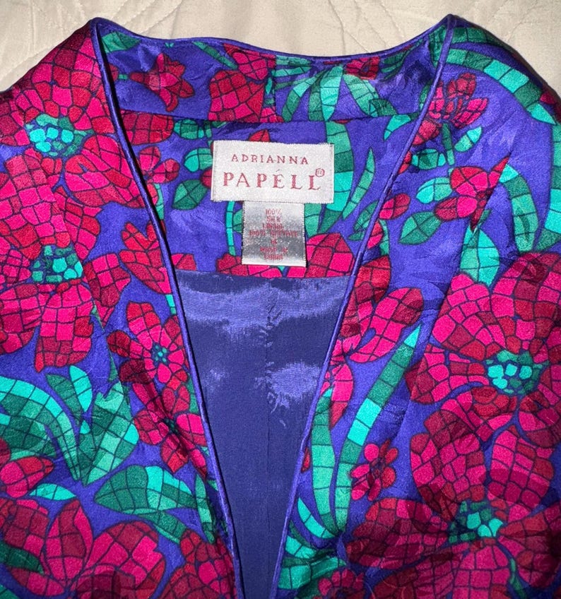 Peut inclure: Veste aux motifs floraux vibrants dans les tons de violet, fuchsia et sarcelle. La veste pr&eacute;sente une encolure en V et un imprim&eacute; floral audacieux. L'&eacute;tiquette indique "Adrianna Papell".