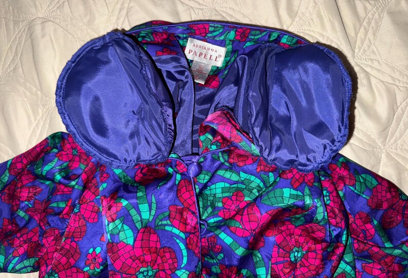 Peut inclure: Veste vintage Adrianna Papell &agrave; motifs floraux vibrants. La veste pr&eacute;sente une base violet fonc&eacute; avec de grands motifs floraux roses et verts. Le col et la doublure sont bleu roi uni. La veste a une fermeture boutonn&eacute;e.