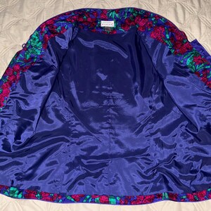 Peut inclure: Veste vintage ouverte avec un motif floral. L'int&eacute;rieur est bleu fonc&eacute;, contrastant avec le motif floral color&eacute; rose, vert et bleu sur les bords. La veste est faite d'une mati&egrave;re soyeuse.