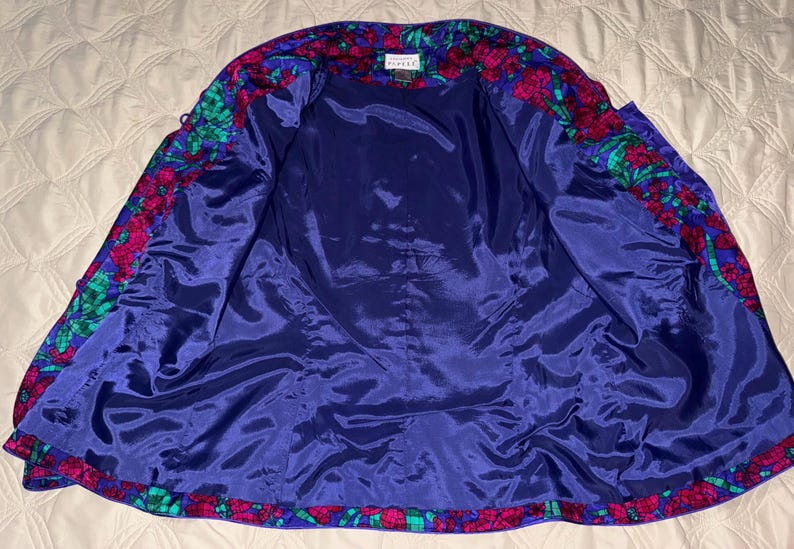 Peut inclure: Veste vintage ouverte avec un motif floral. L'int&eacute;rieur est bleu fonc&eacute;, contrastant avec le motif floral color&eacute; rose, vert et bleu sur les bords. La veste est faite d'une mati&egrave;re soyeuse.
