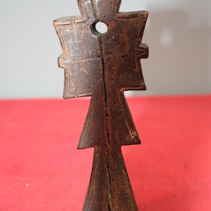 May include: A dark brown wooden cross with a hole in the center. The cross is carved with intricate details and has a pointed bottom.