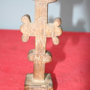 May include: A wooden cross with a carved figure of Jesus Christ on the front. The cross has a base and is decorated with carvings. The letters "HK" and "MX" are carved into the wood.