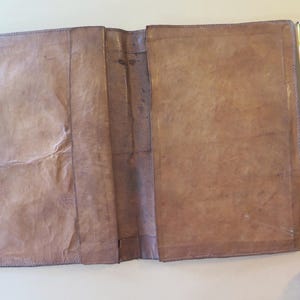 K&ouml;nnte beinhalten: Offenes, braunes Lederjournal mit abgenutztem Aussehen. Das Journal ist ge&ouml;ffnet und zeigt leere Seiten. Ein gelbes Ma&szlig;band liegt neben dem Journal und zeigt eine L&auml;nge von etwa 30 cm.