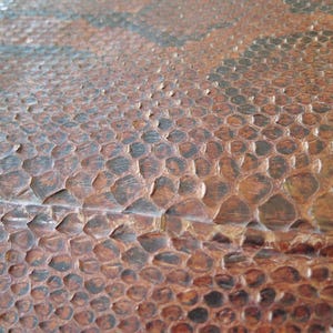 K&ouml;nnte beinhalten: Nahaufnahme einer strukturierten Oberfl&auml;che mit einem sich wiederholenden Muster aus braunen und schwarzen Schuppen. Die Schuppen haben eine erhabene, unebene Textur, und der Gesamteffekt erinnert an Reptilienhaut.