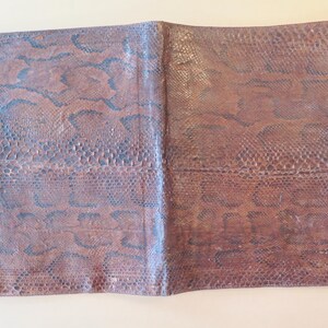 K&ouml;nnte beinhalten: Offenes, braunes Leder-Notizbuch mit Schlangenmuster. Das Notizbuch ist ge&ouml;ffnet und zeigt das Innere. Das Leder hat ein strukturiertes Aussehen mit dunkelblauen und braunen T&ouml;nen. Das Notizbuch ist rechteckig.