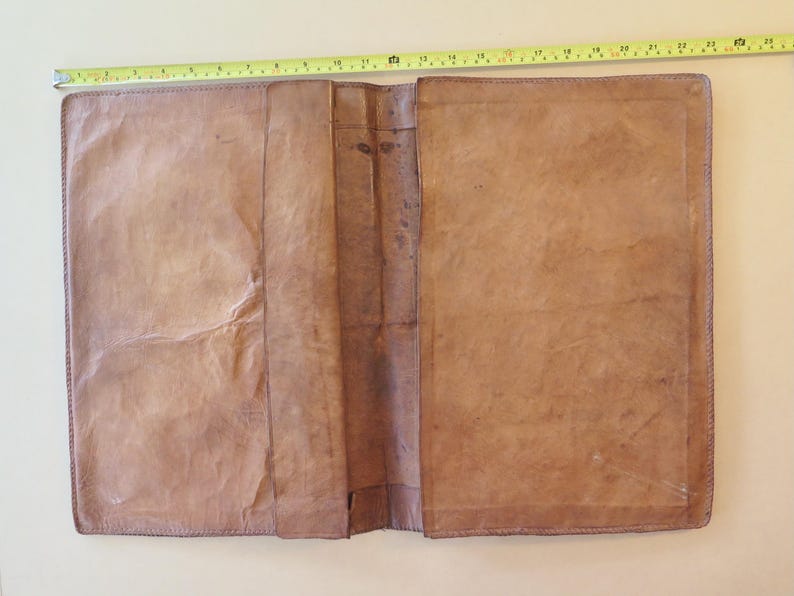 K&ouml;nnte beinhalten: Offenes, braunes Lederjournal mit einer gen&auml;hten Bord&uuml;re. Das Journal ist im ge&ouml;ffneten Zustand etwa 61 cm lang und 41 cm breit. Das Leder hat ein abgenutztes, strukturiertes Aussehen mit sichtbaren Falten und Farbvariationen.